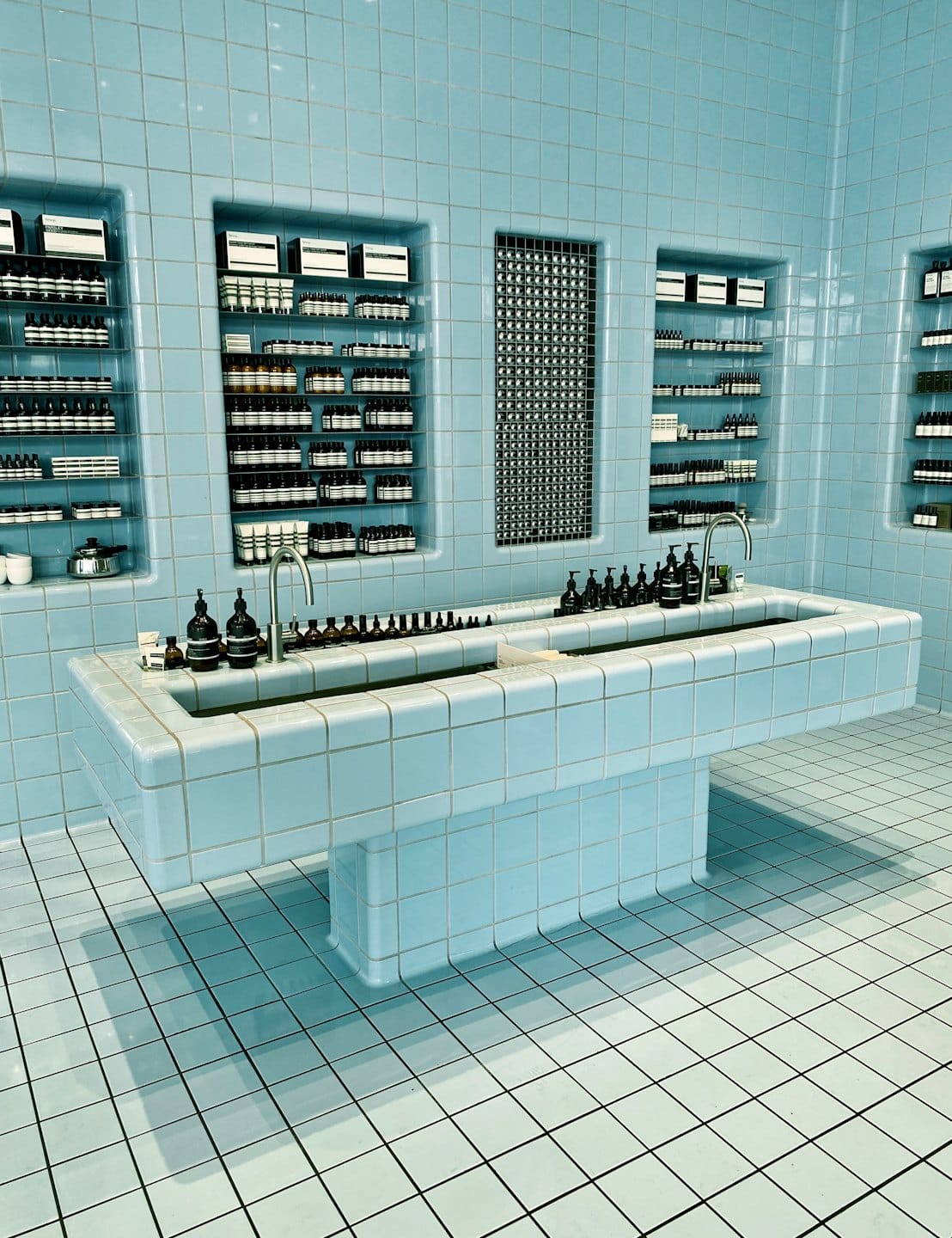 Skincare products arranged on blue tiled shelves and a sink.